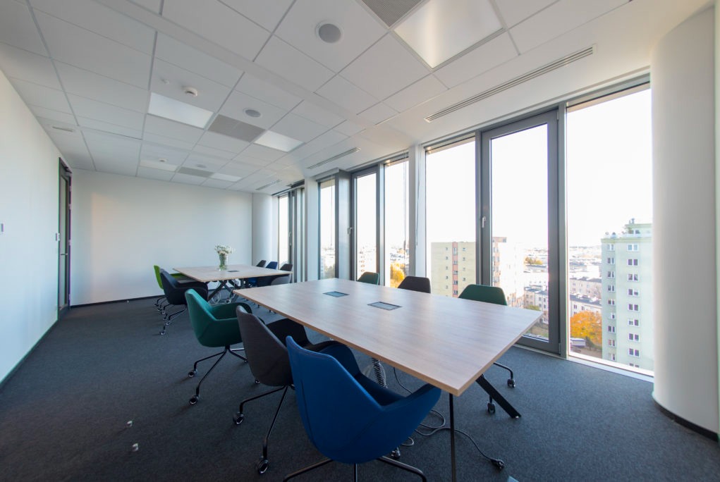 Jasne, nowoczesne biuro z dużymi oknami, widokiem na miasto, stołami konferencyjnymi z wbudowanymi gniazdami i ergonomicznymi krzesłami na kółkach.