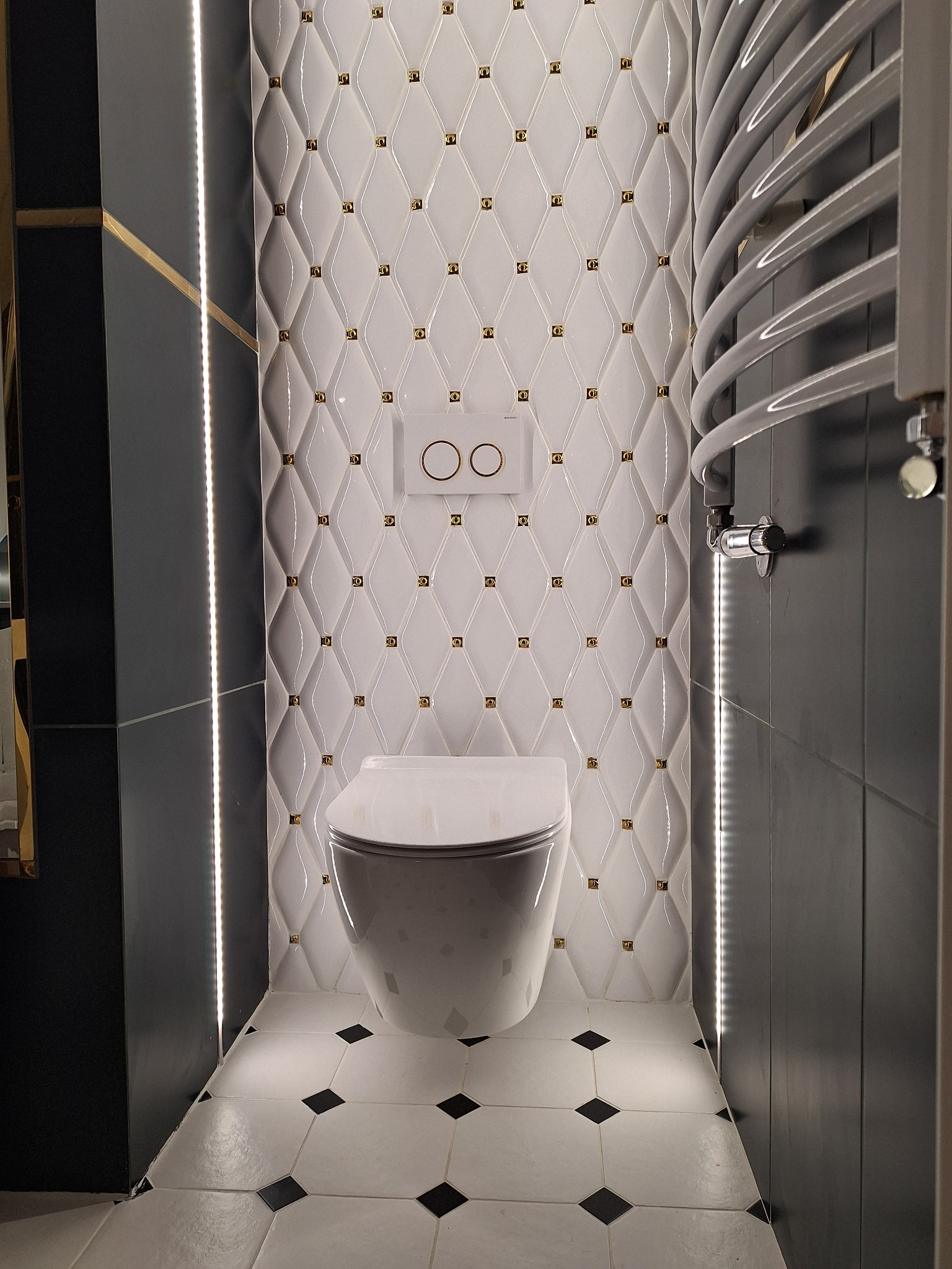 Nowoczesna toaleta podwieszana z białą, pikowaną ścianą z akcentami w kolorze złota, czarnymi panelami bocznymi z oświetleniem LED i grzejnikiem drabinkowym.