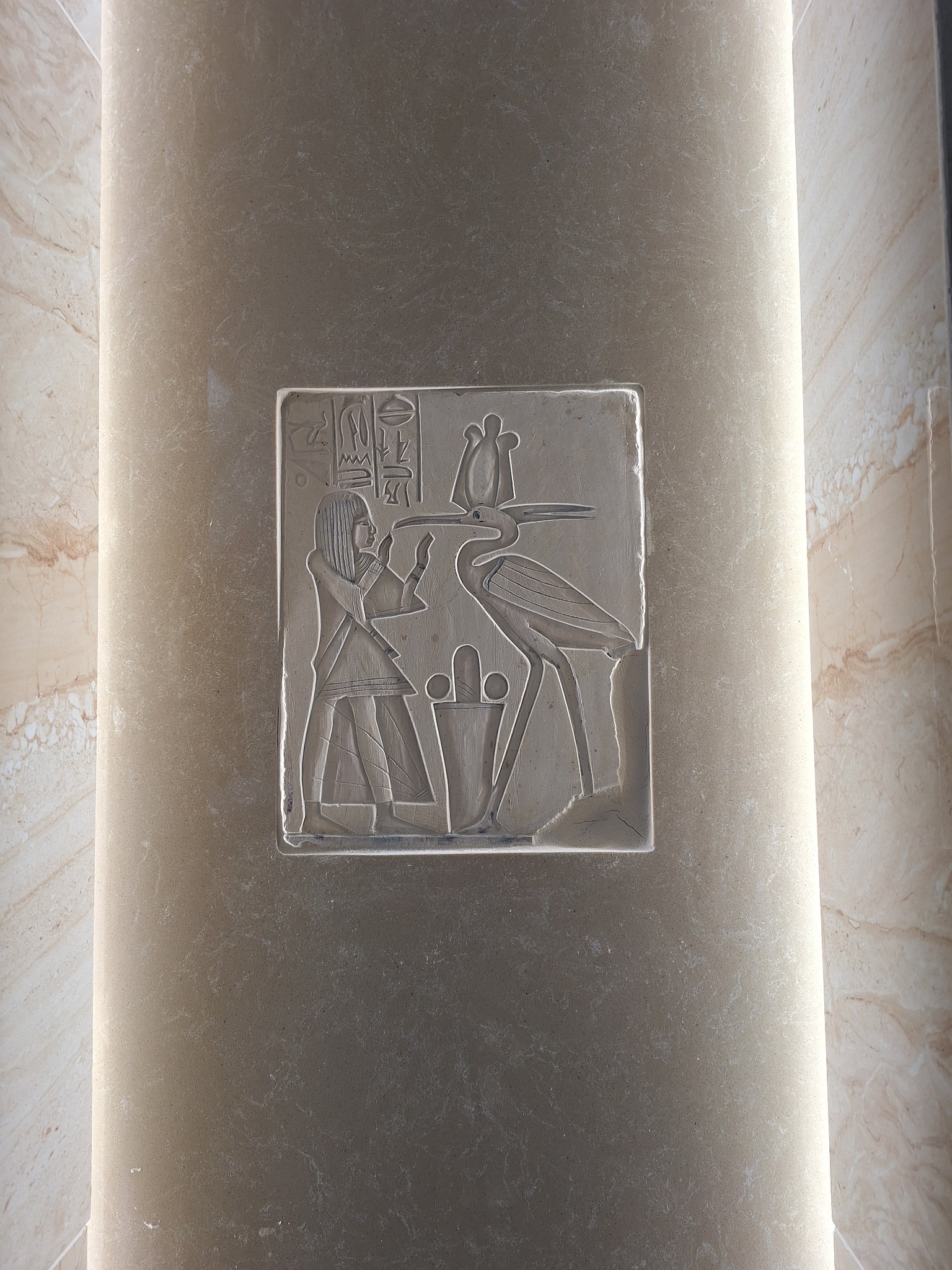 Płaskorzeźba z motywem starożytnego Egiptu, przedstawiająca postać ludzką i ptaka, umieszczona na kolumnie z podświetleniem LED, stanowiąca element dekoracyjny wnętrza.