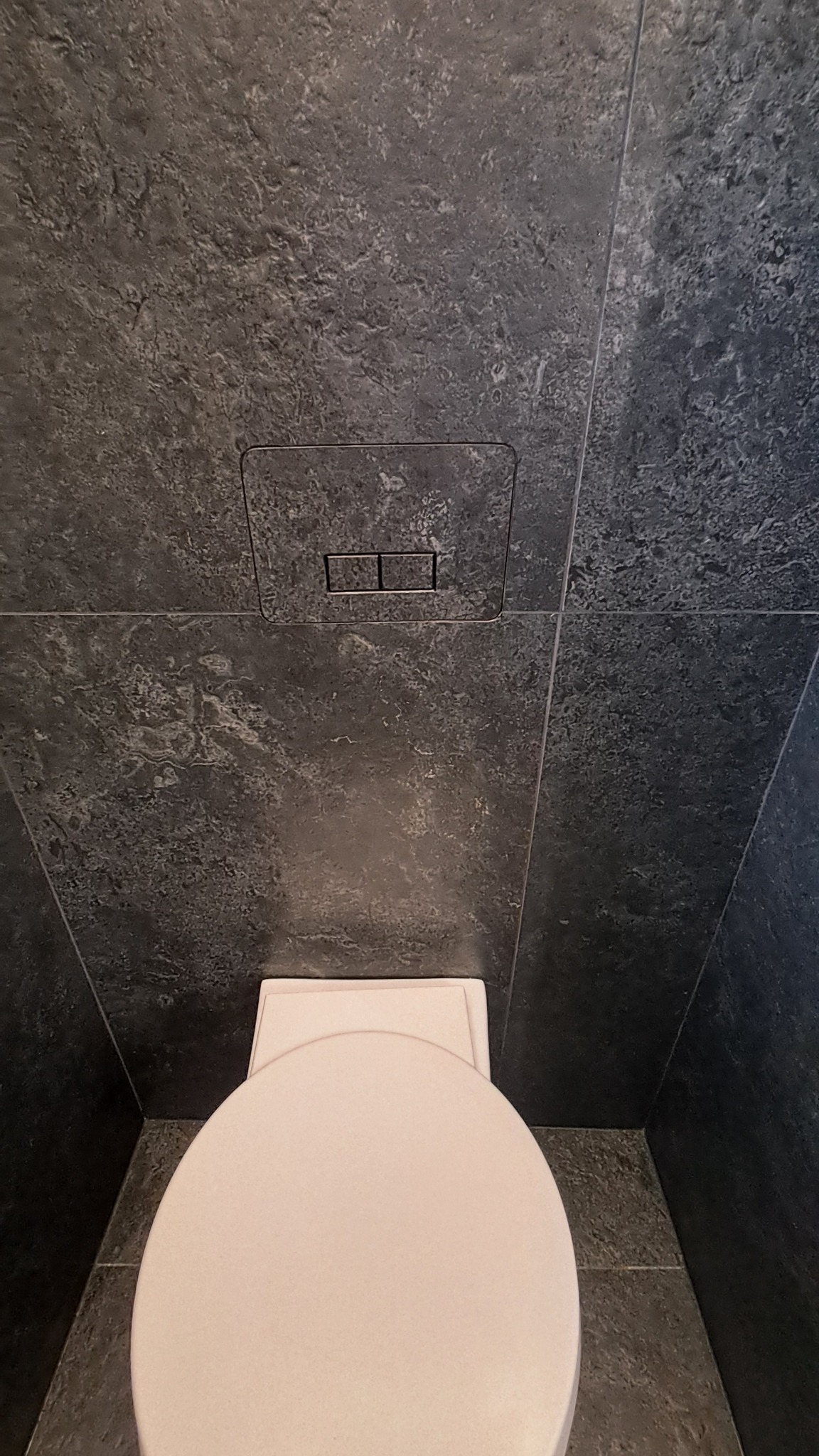 Nowoczesna toaleta z czarnymi płytkami imitującymi kamień, widok z góry. Minimalistyczny design z ukrytym systemem spłukiwania.