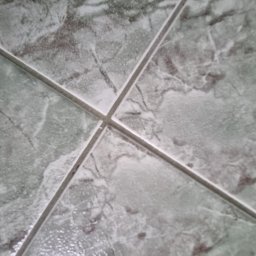 Serwis Sprzątający W Porządku - Szczegółowe ujęcie szaro-zielonych płytek podłogowych z wyraźnym wzorem marmurkowym i fugami, ułożonych ukośnie.