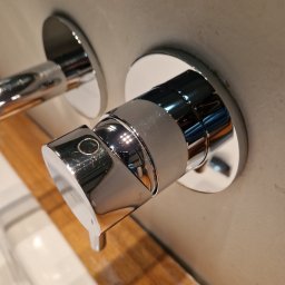 Serwis Sprzątający W Porządku - Błyszcząca chromowana bateria umywalkowa zamontowana na szarej ścianie, z widocznym fragmentem umywalki i blatu z jasnego drewna.