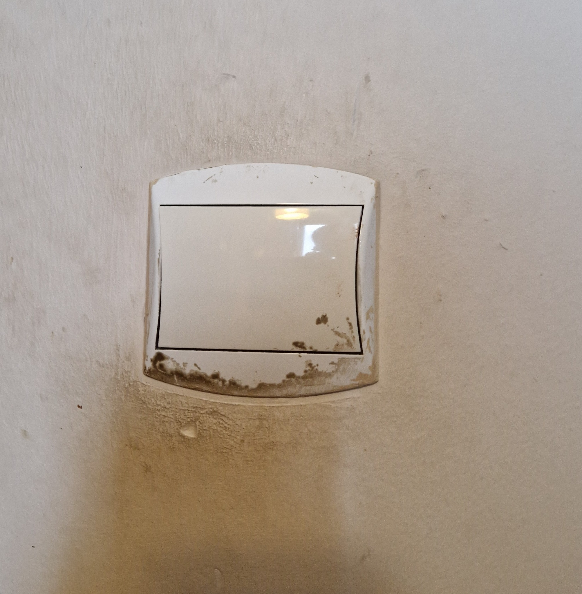 Brudny, biały włącznik światła na ścianie z widocznymi zabrudzeniami i zaciekami.