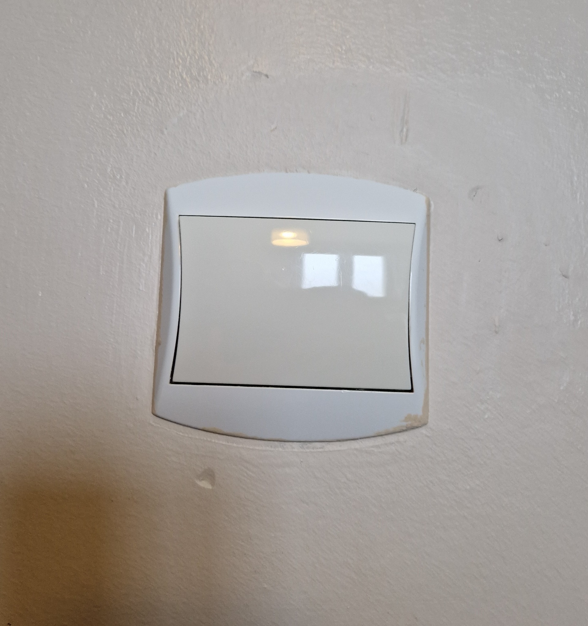Biały, plastikowy włącznik światła na pomalowanej ścianie, widoczne ślady farby i niedoskonałości malowania wokół włącznika.