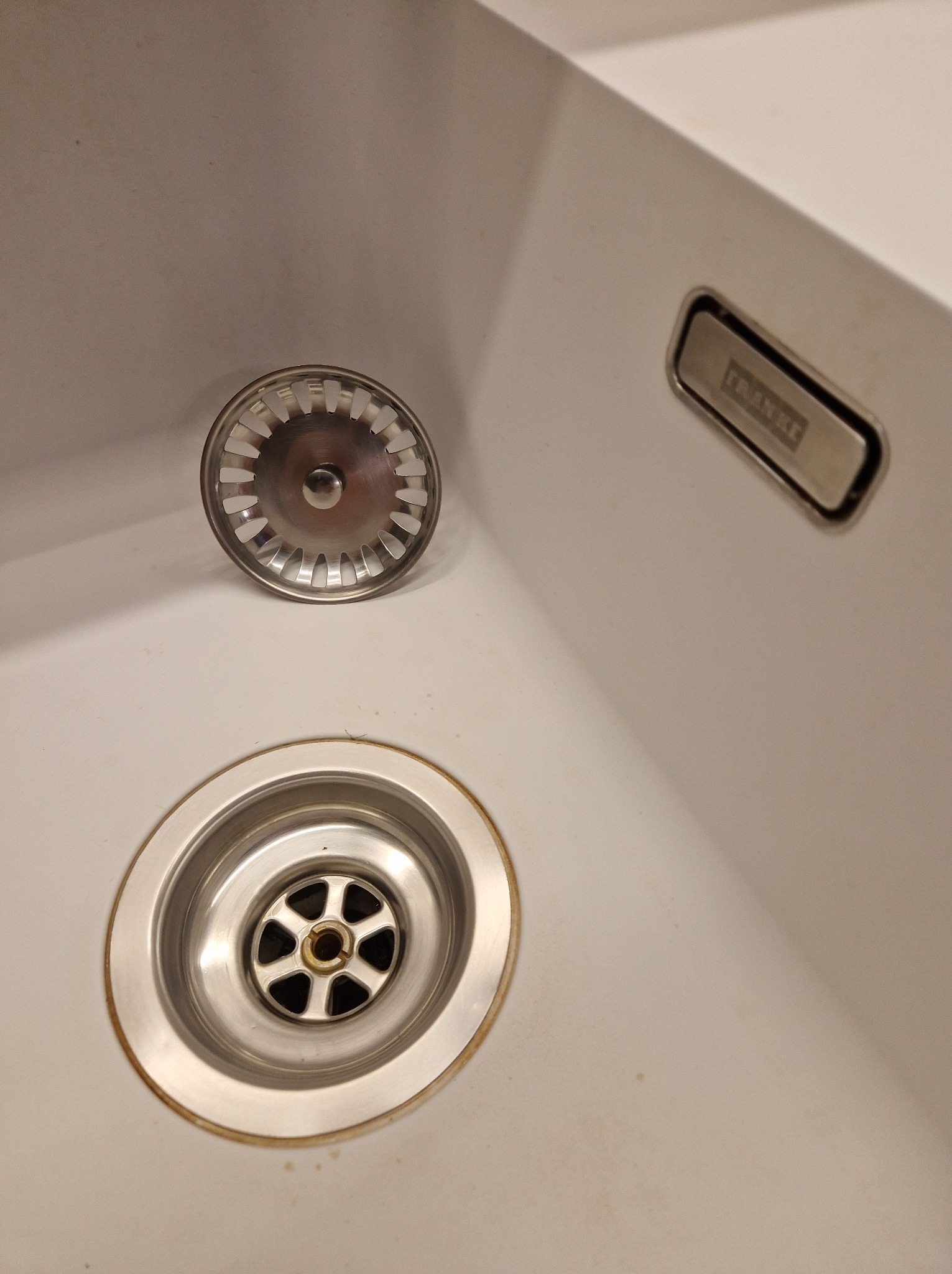 Biały zlew Franke z widocznym odpływem i sitkiem obok, przed czyszczeniem.