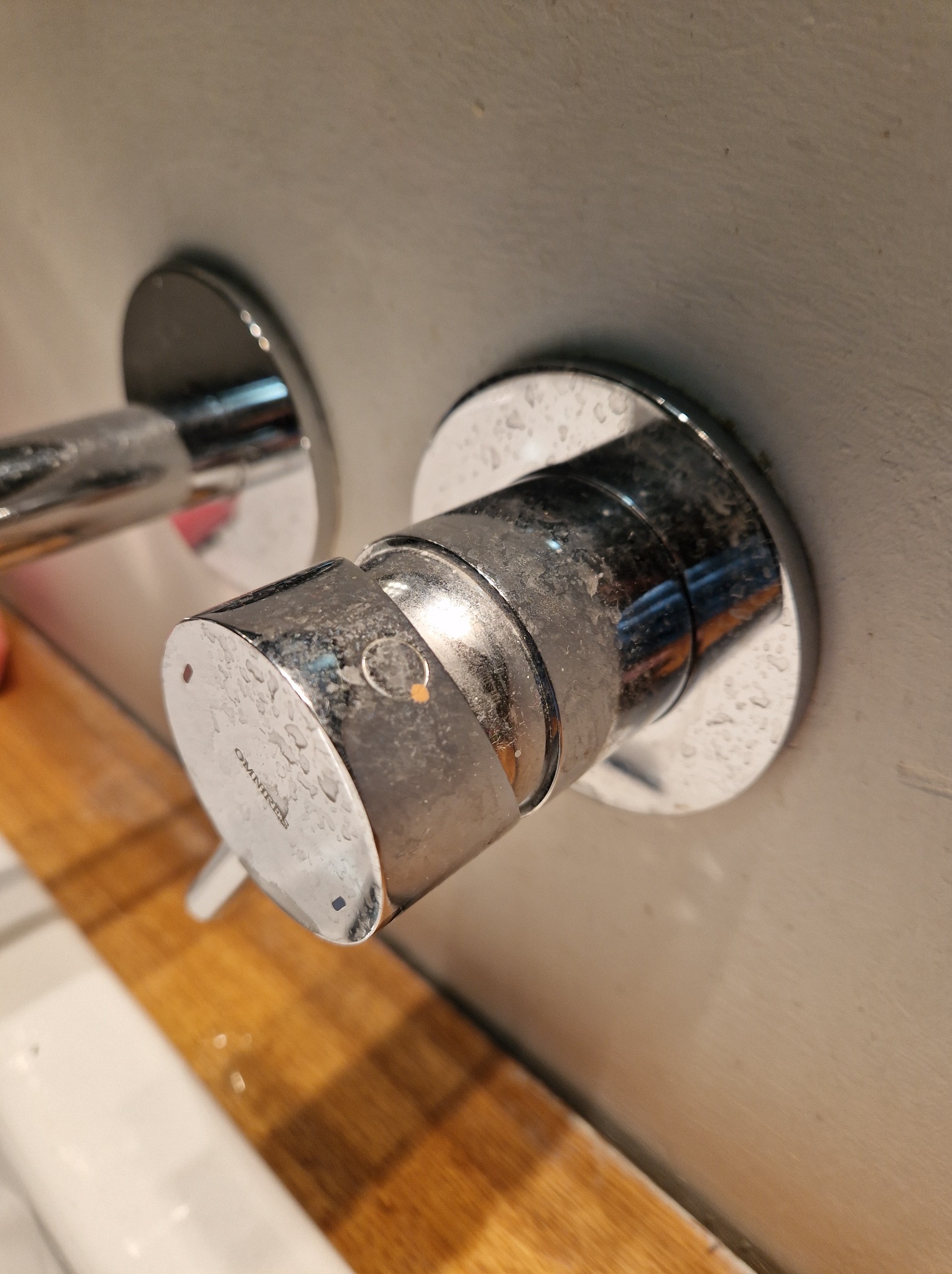 Chromowana bateria umywalkowa z widocznymi śladami zaschniętej wody i osadu, zamontowana na jasnej ścianie nad drewnianym blatem.