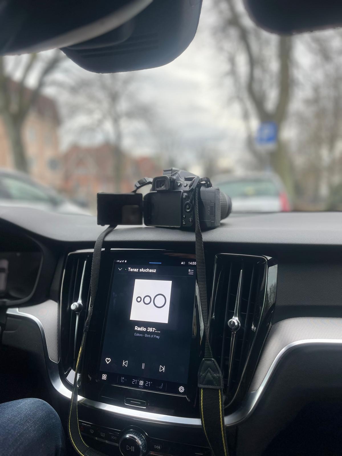 Aparat fotograficzny leży na desce rozdzielczej samochodu, na ekranie radia widać odtwarzaną stację radiową Radio 357.