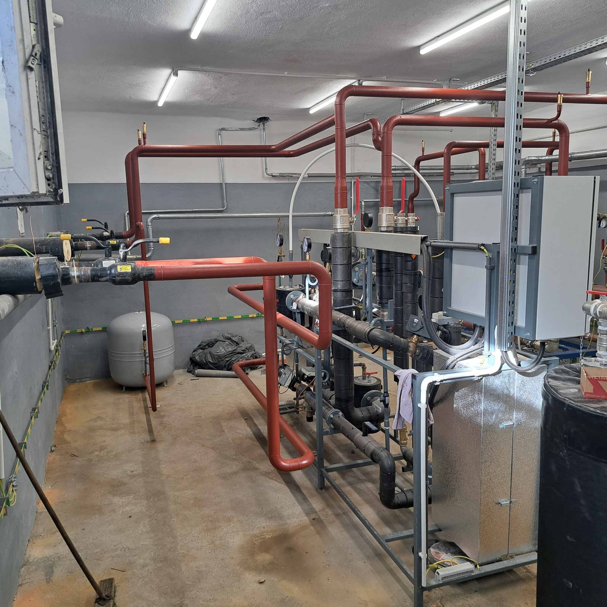 Złożona instalacja rurowa z licznymi zaworami, manometrami i elementami sterującymi, zamontowana w pomieszczeniu technicznym z widocznymi elementami konstrukcyjnymi budynku i oświetleniem