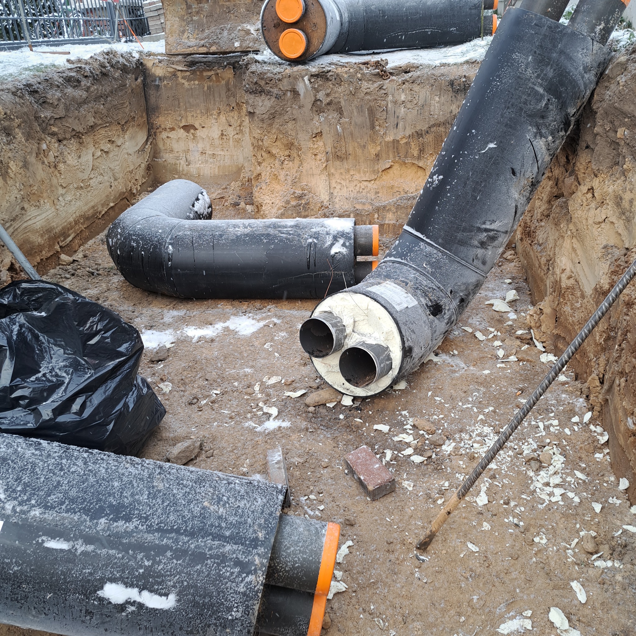 Rury ciepłownicze w wykopie, pokryte szronem, z widoczną izolacją i elementami montażowymi, przygotowane do spawania.