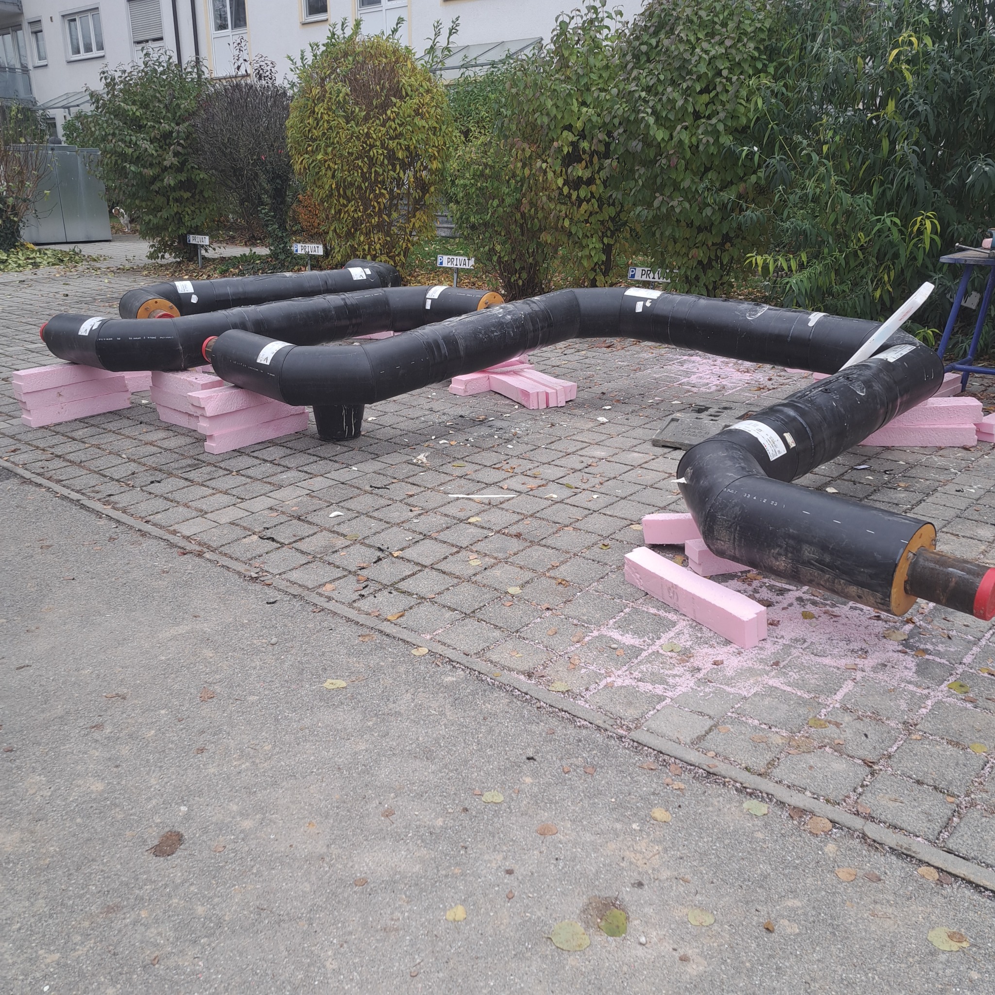 Czarne rury izolowane termicznie, ułożone na różowych blokach styropianowych na zewnątrz budynku w Olsztynie, prawdopodobnie przygotowane do montażu.