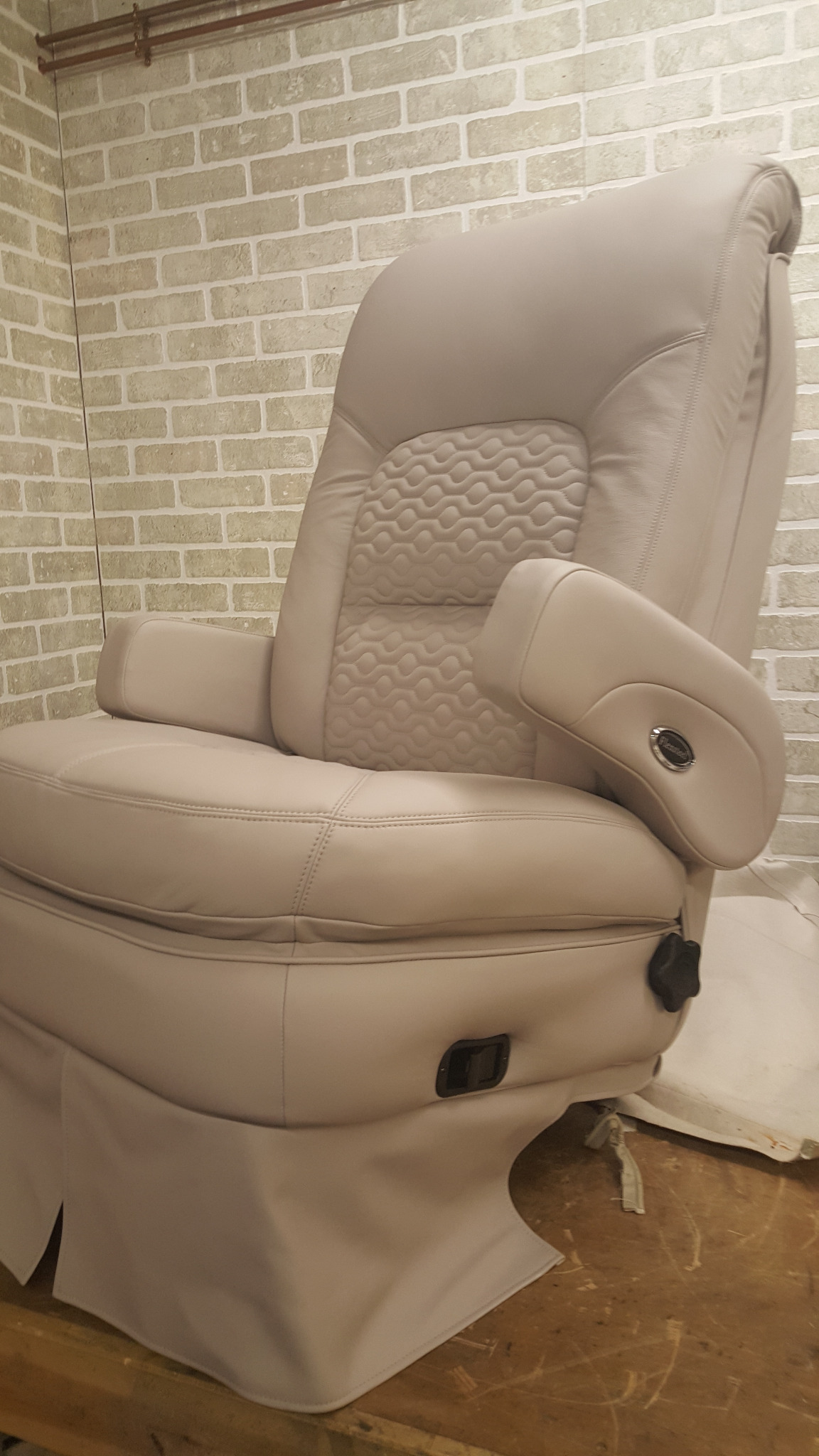 Beżowy fotel z podłokietnikami, tapicerowany skórą z wzorem na oparciu, na tle ściany z cegieł.