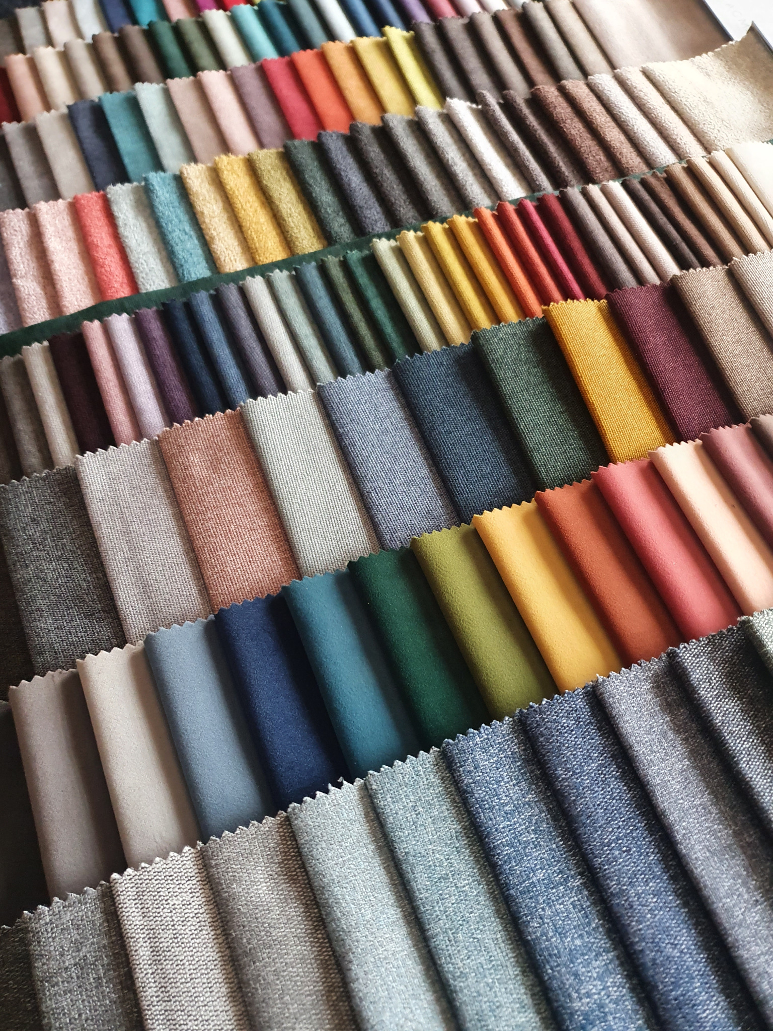 Paleta próbek tkanin tapicerskich w różnych kolorach i fakturach ułożonych rzędami, widoczne krawędzie ząbkowane.