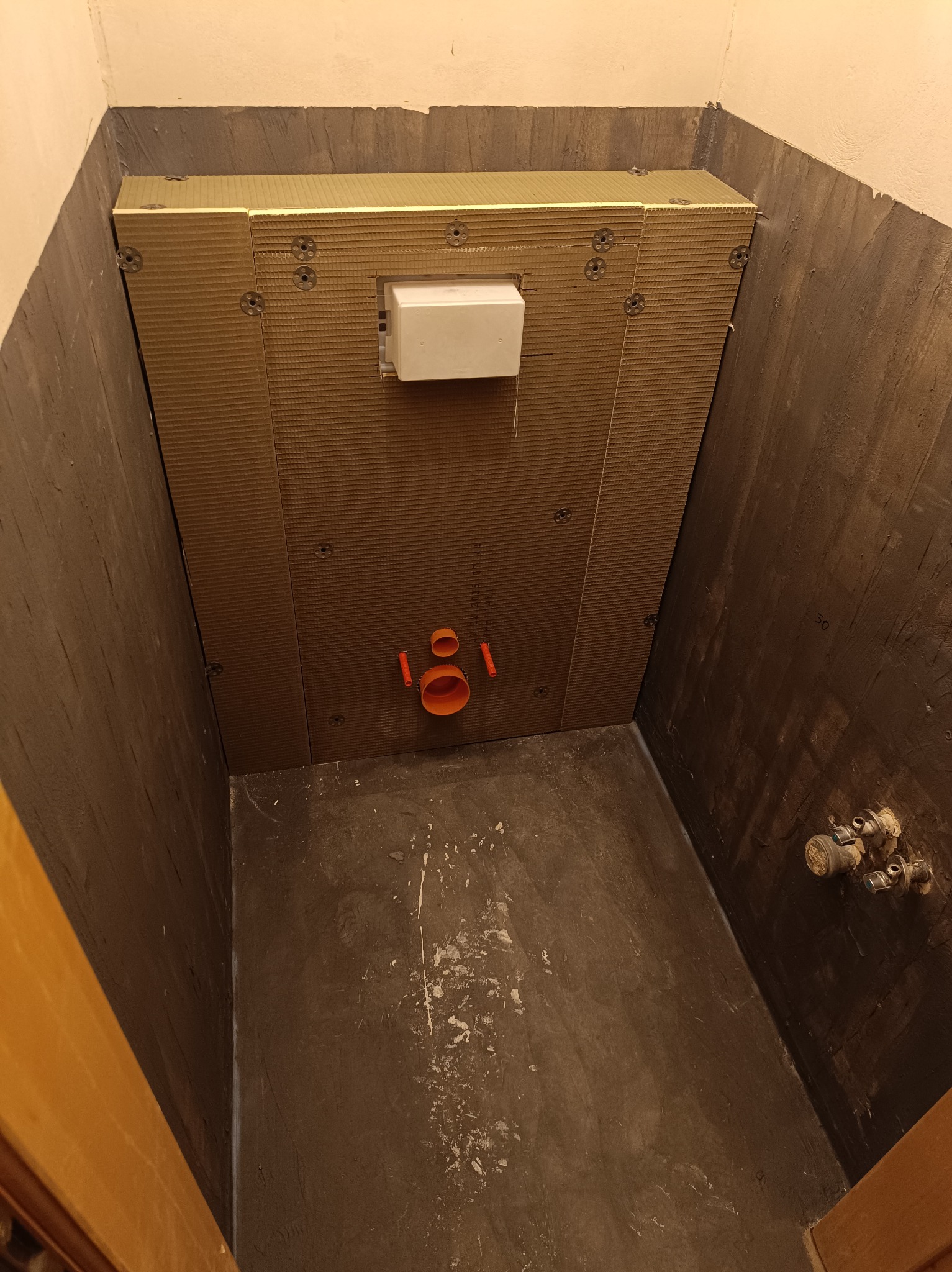 Montaż stelaża podtynkowego WC z widocznymi przyłączami kanalizacyjnymi i wodnymi na tle surowych ścian łazienki przed wykończeniem.