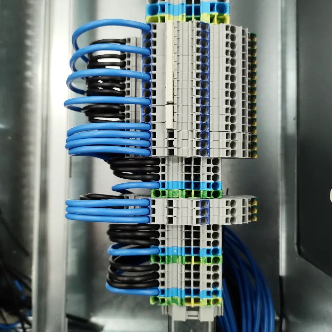 Szczegółowe ujęcie panelu elektrycznego z precyzyjnie ułożonymi przewodami w kolorach niebieskim i czarnym, wpiętymi w listwy zaciskowe o zróżnicowanej kolorystyce.