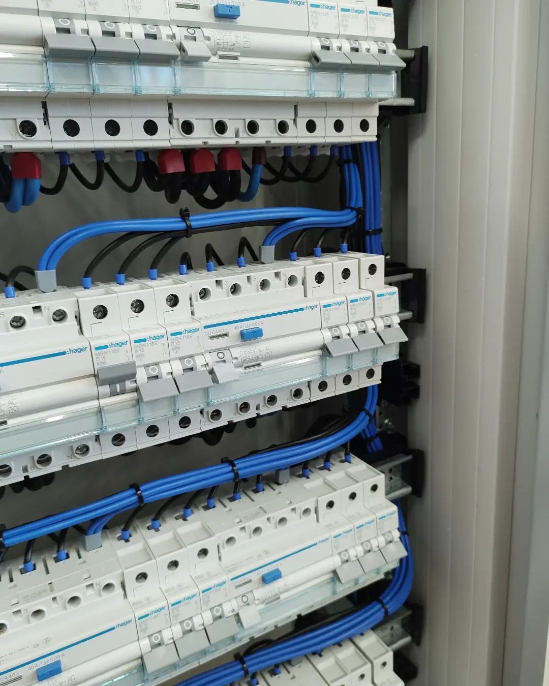 Rozdzielnica elektryczna Hager z bezpiecznikami i niebieskimi przewodami. Widoczne elementy montażowe i oznaczenia na urządzeniach.