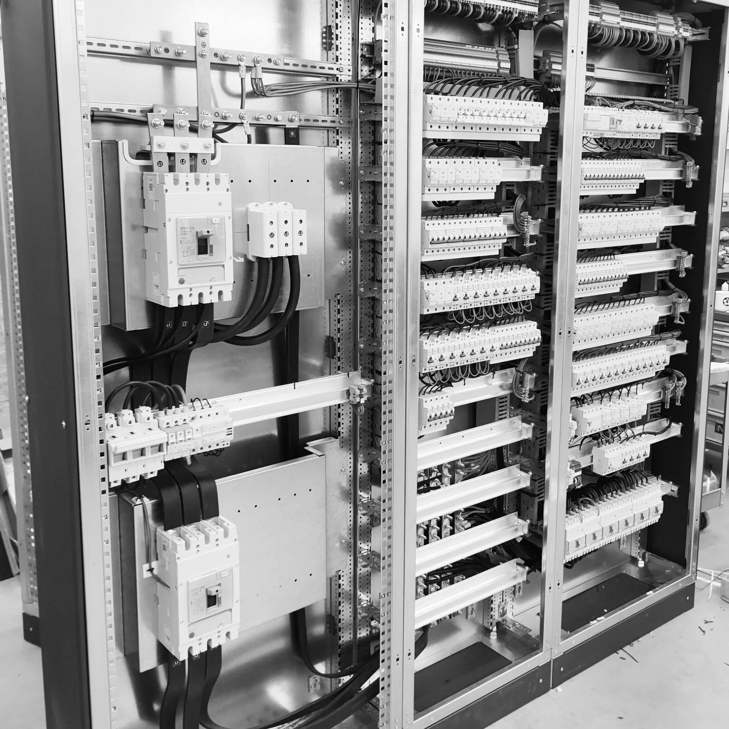 Rozbudowana szafa elektryczna w odcieniach szarości, ukazująca liczne zabezpieczenia, przewody i listwy zaciskowe. Precyzyjny montaż widoczny wewnątrz metalowej obudowy.