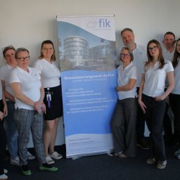 Zespół biura rachunkowego Fik Finanse i Księgowość pozuje na tle roll-upu z nowoczesnym budynkiem biurowym i hasłem 'Nowoczesna księgowość dla firm'.