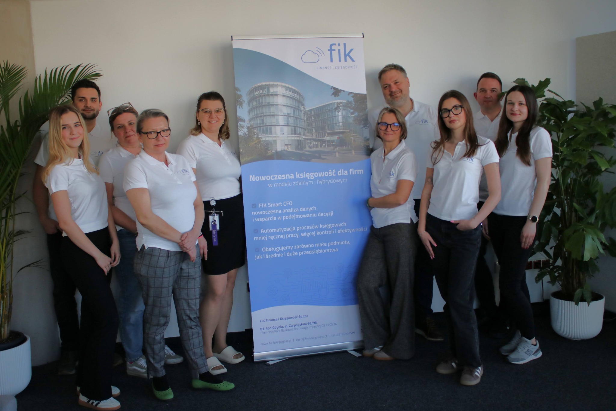Zespół biura rachunkowego Fik Finanse i Księgowość pozuje na tle roll-upu z nowoczesnym budynkiem biurowym i hasłem 'Nowoczesna księgowość dla firm'.