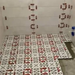 Układanie wzorzystych płytek podłogowych w łazience z użyciem poziomych sznurków i czerwonych klipsów dystansowych na ścianach.