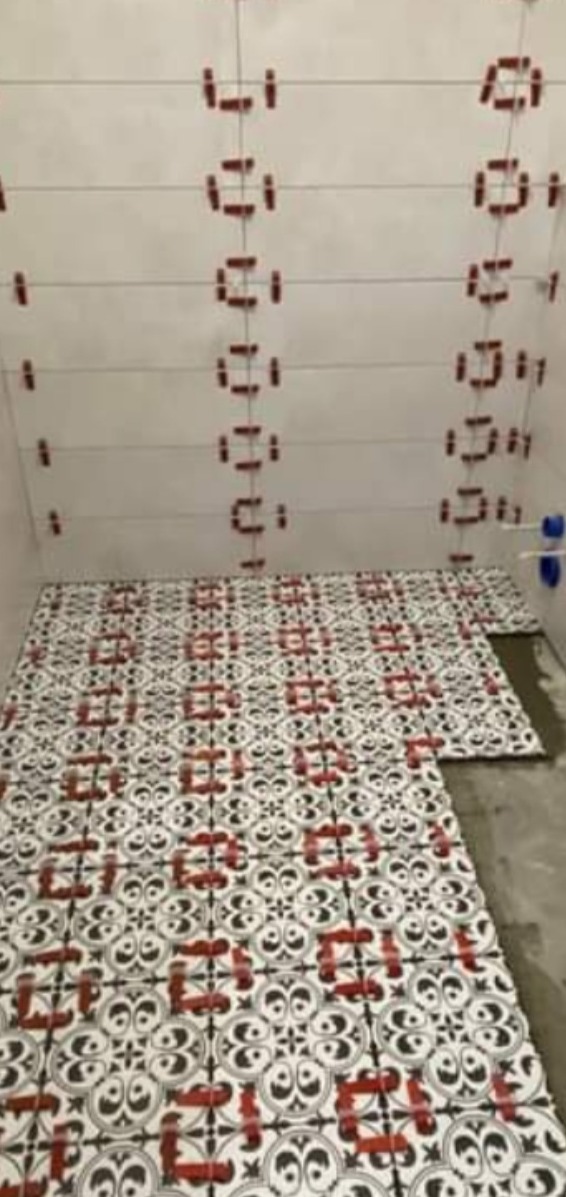 Układanie wzorzystych płytek podłogowych w łazience z użyciem poziomych sznurków i czerwonych klipsów dystansowych na ścianach.