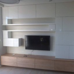 Oksana Shulyar Firma Produkcyjno-Usługowa VIDA MEBBUD - Biała zabudowa meblowa na ścianie z telewizorem, dolne szafki z forniru dębowego, minimalistyczny design.