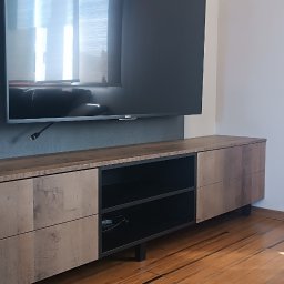 Oksana Shulyar Firma Produkcyjno-Usługowa VIDA MEBBUD - Nowoczesna szafka RTV z drewnianymi frontami i otwartą przestrzenią na sprzęt, wiszący telewizor na szarej ścianie, drewniana podłoga.