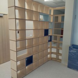 Oksana Shulyar Firma Produkcyjno-Usługowa VIDA MEBBUD - Duża, drewniana, ażurowa szafa na wymiar z elementami w kolorze niebieskim, pełniąca funkcję ścianki działowej w jasnym pomieszczeniu.