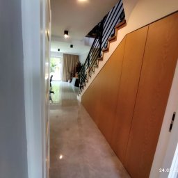 Oksana Shulyar Firma Produkcyjno-Usługowa VIDA MEBBUD - Wnętrze domu z szafą na wymiar pod schodami, drewniane fronty bez uchwytów, czarne metalowe schody, marmurowe płytki podłogowe.