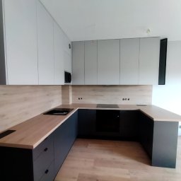 Oksana Shulyar Firma Produkcyjno-Usługowa VIDA MEBBUD - Nowoczesna kuchnia z zabudową w kolorach bieli i grafitu, drewniany blat, płyta indukcyjna, minimalistyczny design.