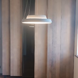 Oksana Shulyar Firma Produkcyjno-Usługowa VIDA MEBBUD - Wysoka zabudowa meblowa z drewnianymi frontami i czarnym, przeszklonym segmentem, oświetlona nowoczesną lampą wiszącą w minimalistycznym wnętrzu z drewnianą podłogą.