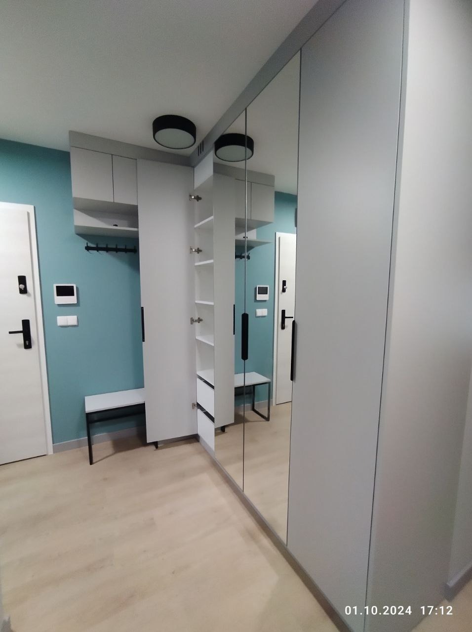 Szara szafa wnękowa z lustrzanymi drzwiami, otwarta z półkami, zintegrowana z siedziskiem w przedpokoju z turkusową ścianą.