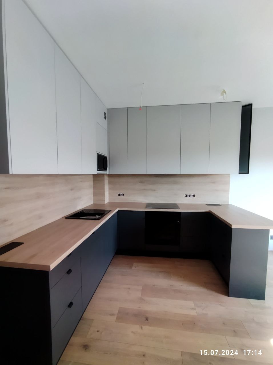 Nowoczesna kuchnia z zabudową w kolorach bieli i grafitu, drewniany blat, płyta indukcyjna, minimalistyczny design.