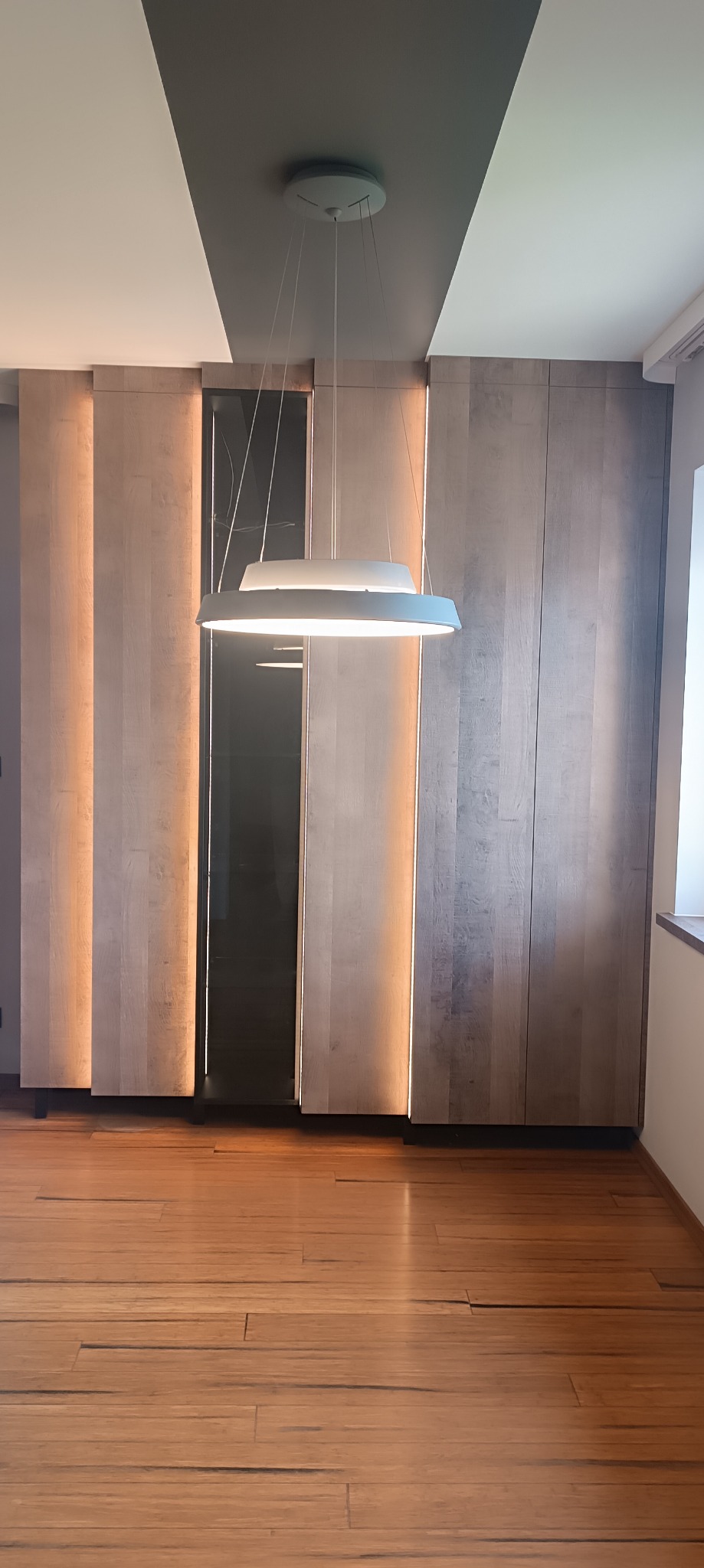 Nowoczesna szafa wnękowa z oświetleniem LED w Krakowie, widoczna z perspektywy podłogi z drewnianych paneli, z wiszącą lampą.
