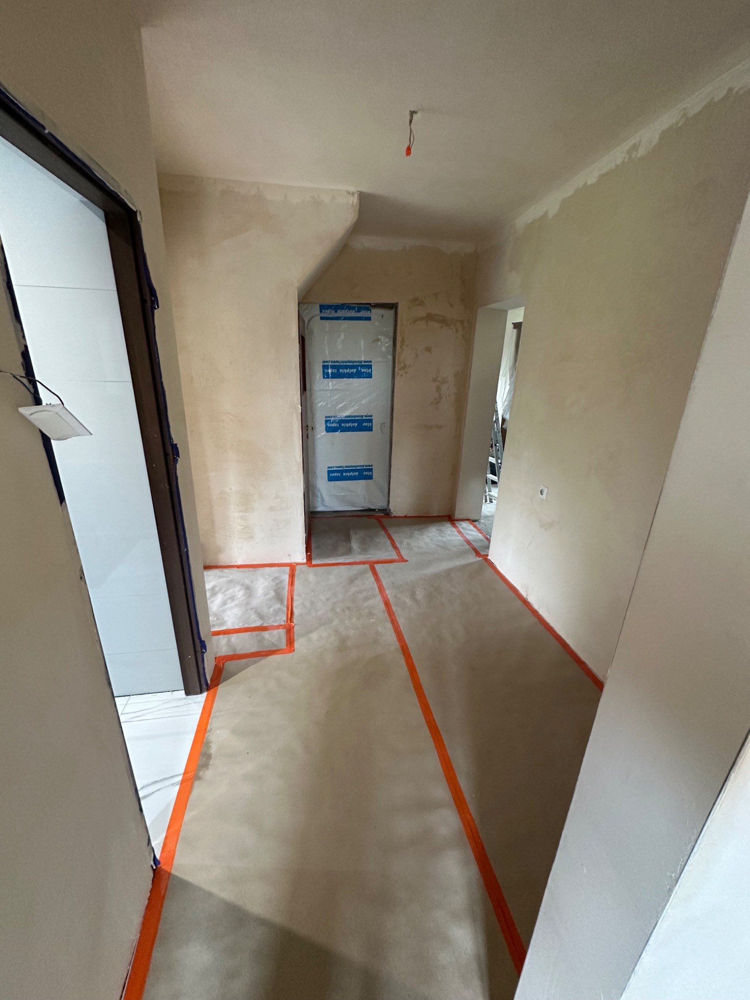 Przygotowanie do malowania w Ostrowi Mazowieckiej: zabezpieczona podłoga taśmą, ściany po szpachlowaniu, drzwi oklejone folią ochronną. Gotowość do dalszych prac wykończeniowych.