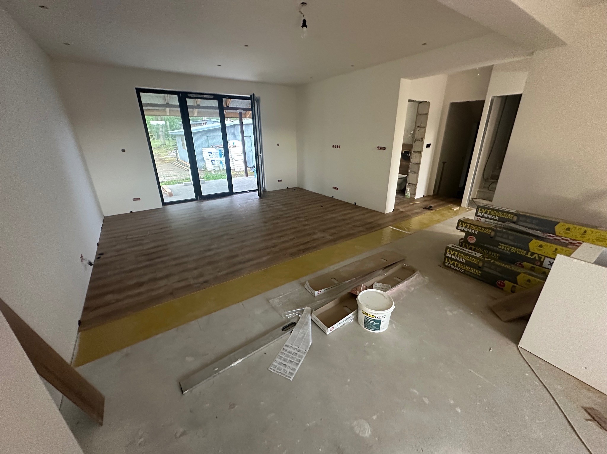 Układanie paneli podłogowych w przestronnym wnętrzu. Częściowo ułożona podłoga z widocznymi narzędziami i materiałami przygotowanymi do dalszych prac wykończeniowych.