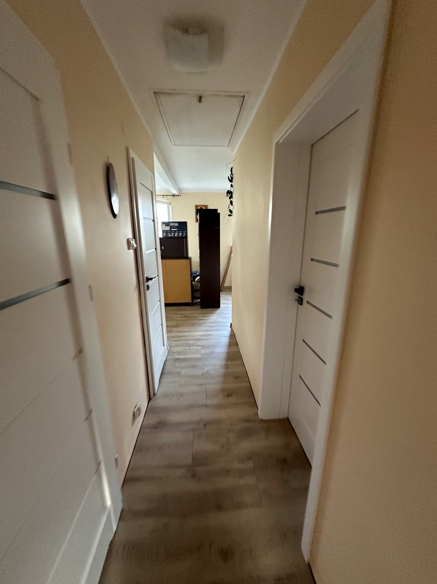 Korytarz po remoncie z panelami podłogowymi i białymi drzwiami z poziomymi, szarymi wstawkami. Ściany w odcieniach beżu. Widok w głąb mieszkania.