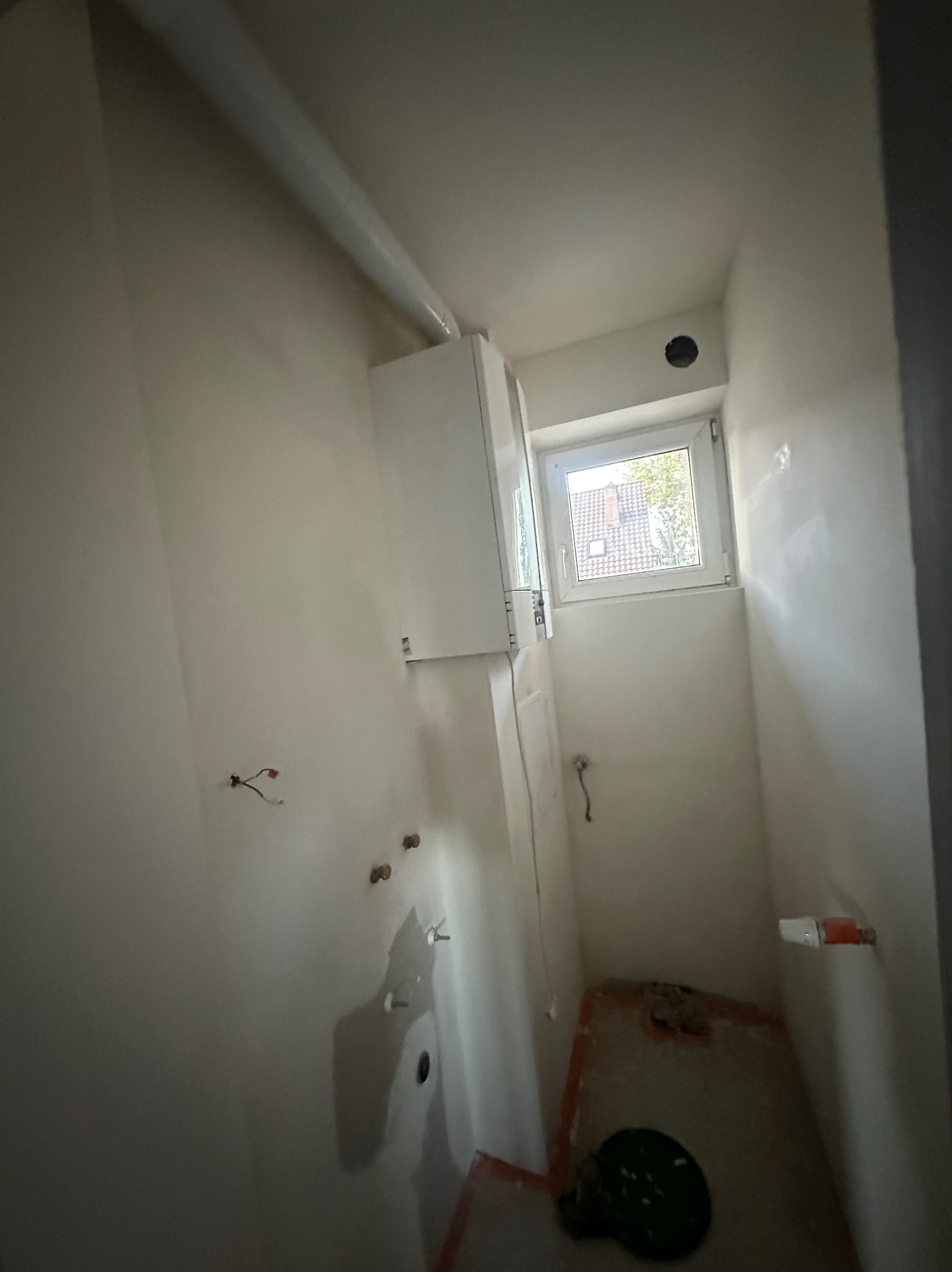 Wnętrze łazienki w trakcie remontu: ściany po szpachlowaniu, widoczne instalacje, okno z widokiem na zewnątrz. Przygotowanie do dalszych prac wykończeniowych.