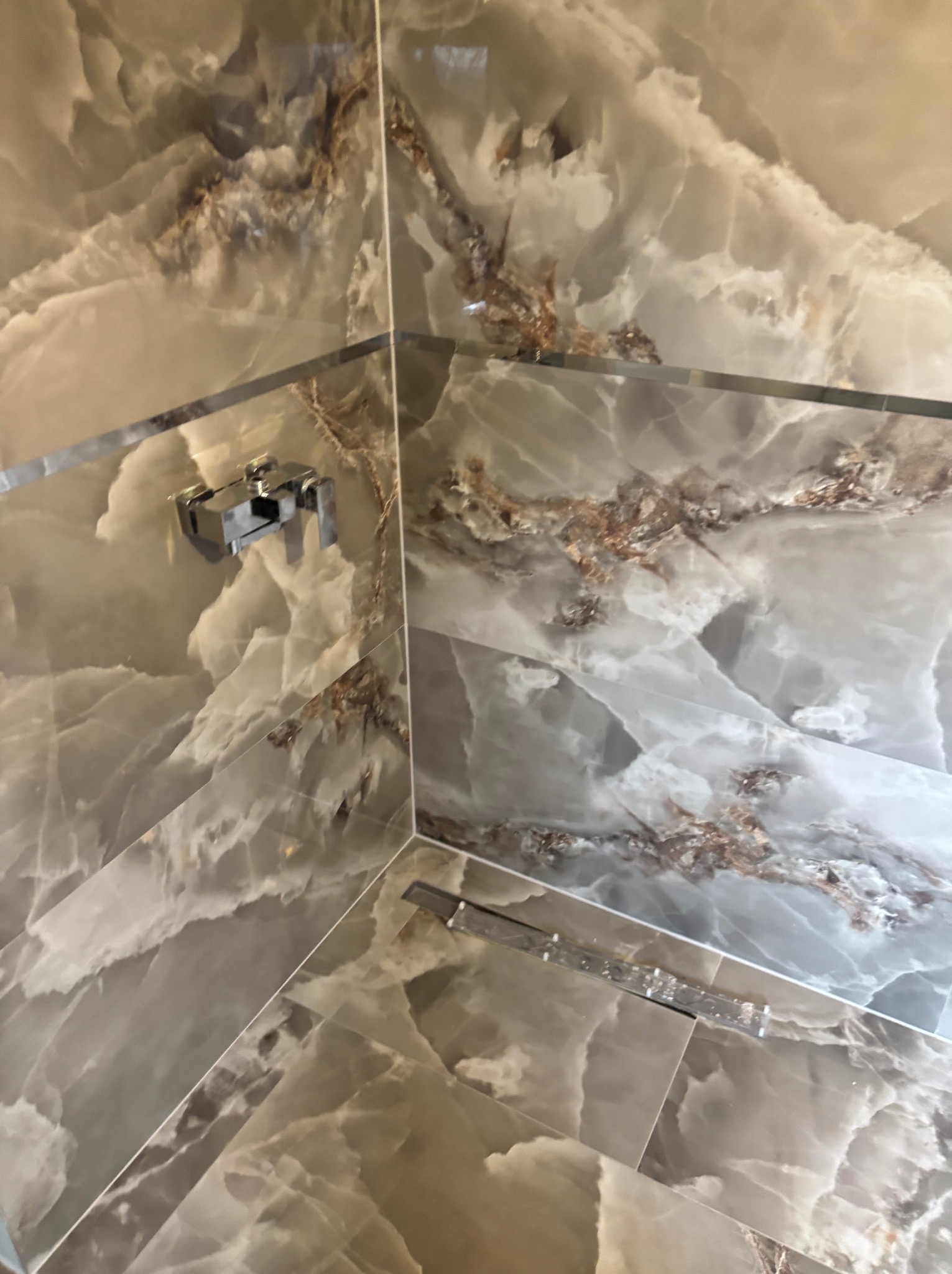 Wykończona kabina prysznicowa z marmurowymi płytkami w odcieniach szarości i brązu, widoczna armatura i odpływ liniowy. Estetyczne połączenie materiałów i dbałość o detale.