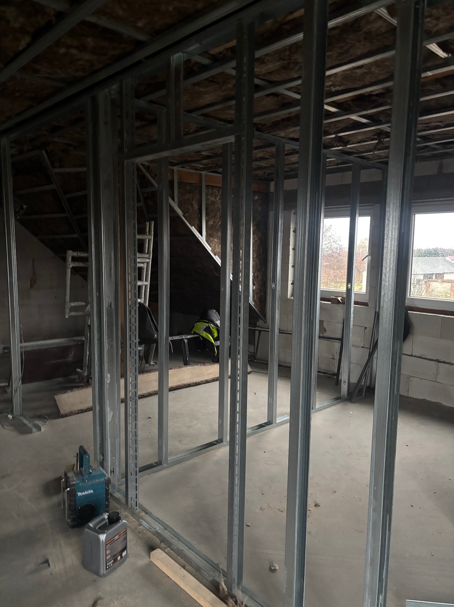 Metalowa konstrukcja ścian działowych z płyty karton-gips w surowym wnętrzu. Widoczne narzędzia i materiały budowlane, okno w tle. Etap prac wykończeniowych.