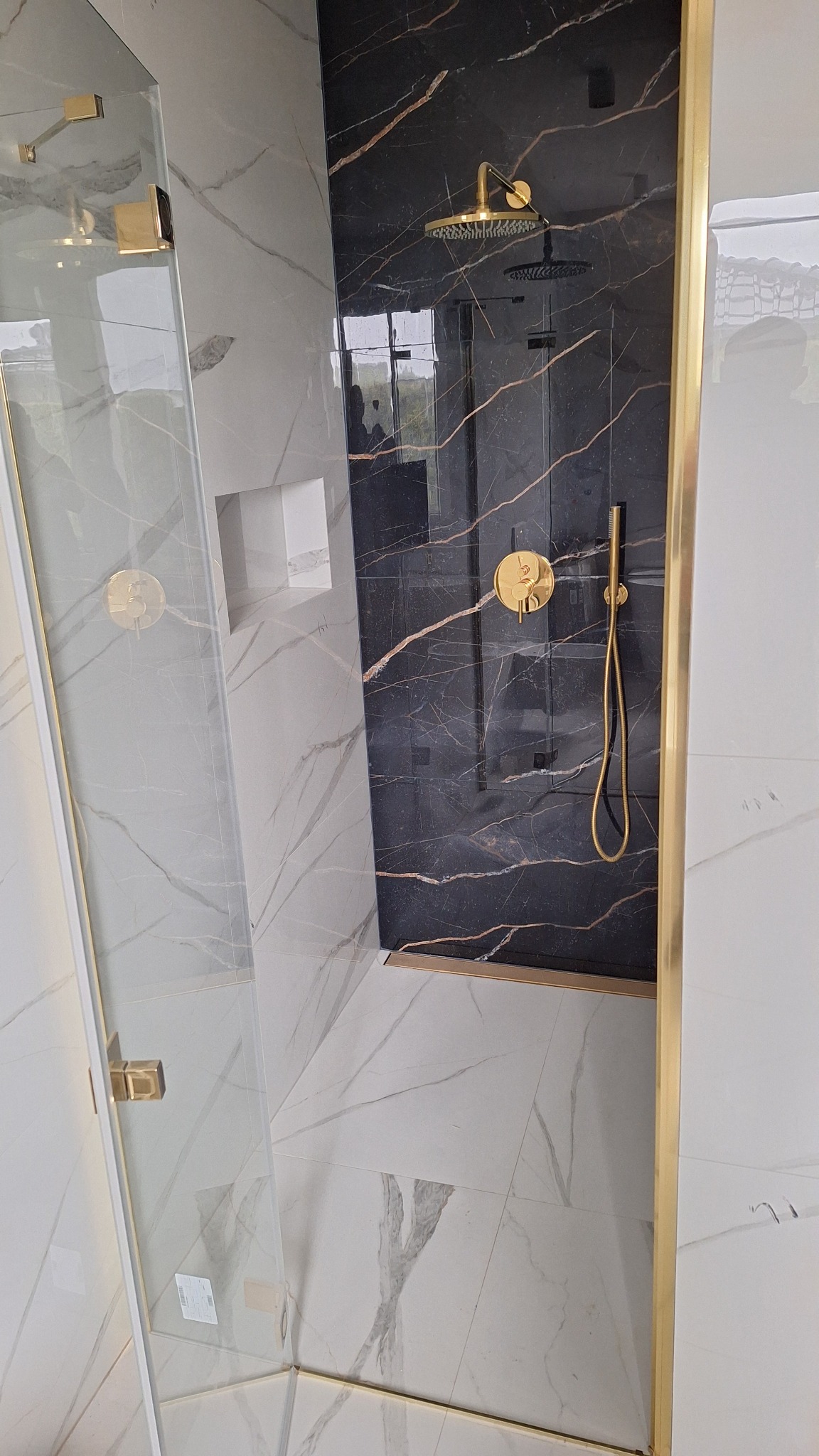 Nowoczesna kabina prysznicowa z marmurowymi płytami w odcieniach bieli i czerni, złota armatura i detale wykończeniowe. Minimalistyczny design, widok z góry.