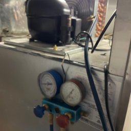 Igor Kupriianow - Agregat chłodniczy z podłączonymi manometrami serwisowymi, widoczny wentylator skraplacza, słabe oświetlenie.