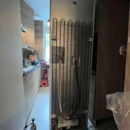 Igor Kupriianow - Tył lodówki z widoczną kratką chłodzącą, podłączona do butli z gazem chłodniczym podczas serwisu w kuchni.