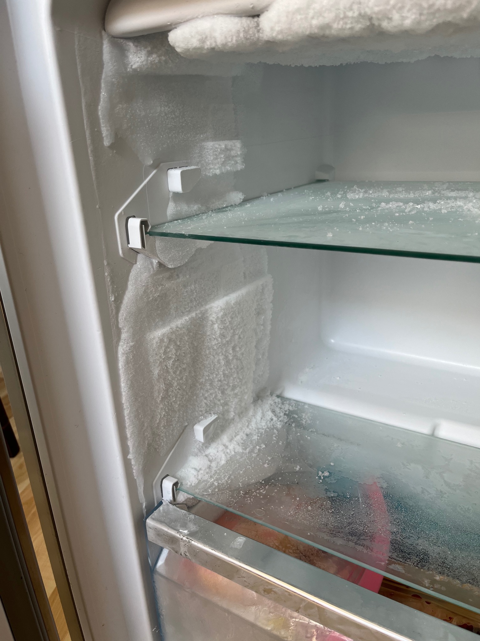 Wnętrze lodówki z grubą warstwą szronu i lodu na ściankach oraz półkach, widoczne kryształki lodu.