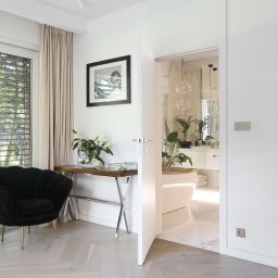 Anna Bartman - Z WNĘTRZA - Nowoczesne wnętrze z czarnym fotelem muszelką na złotych nóżkach, drewnianym stolikiem i otwartymi drzwiami do łazienki z wolnostojącą wanną.