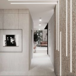 Anna Bartman - Z WNĘTRZA - Nowoczesny korytarz z oświetleniem LED w suficie i na ścianie, z czarno-białym zdjęciem w ramie, prowadzący do salonu z sofą w tle.