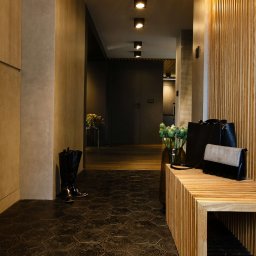 Anna Bartman - Z WNĘTRZA - Nowoczesny przedpokój z drewnianą boazerią, heksagonalną podłogą z wzorem, niską ławką z torebkami, wysokimi butami i bukietami kwiatów w wazonach.