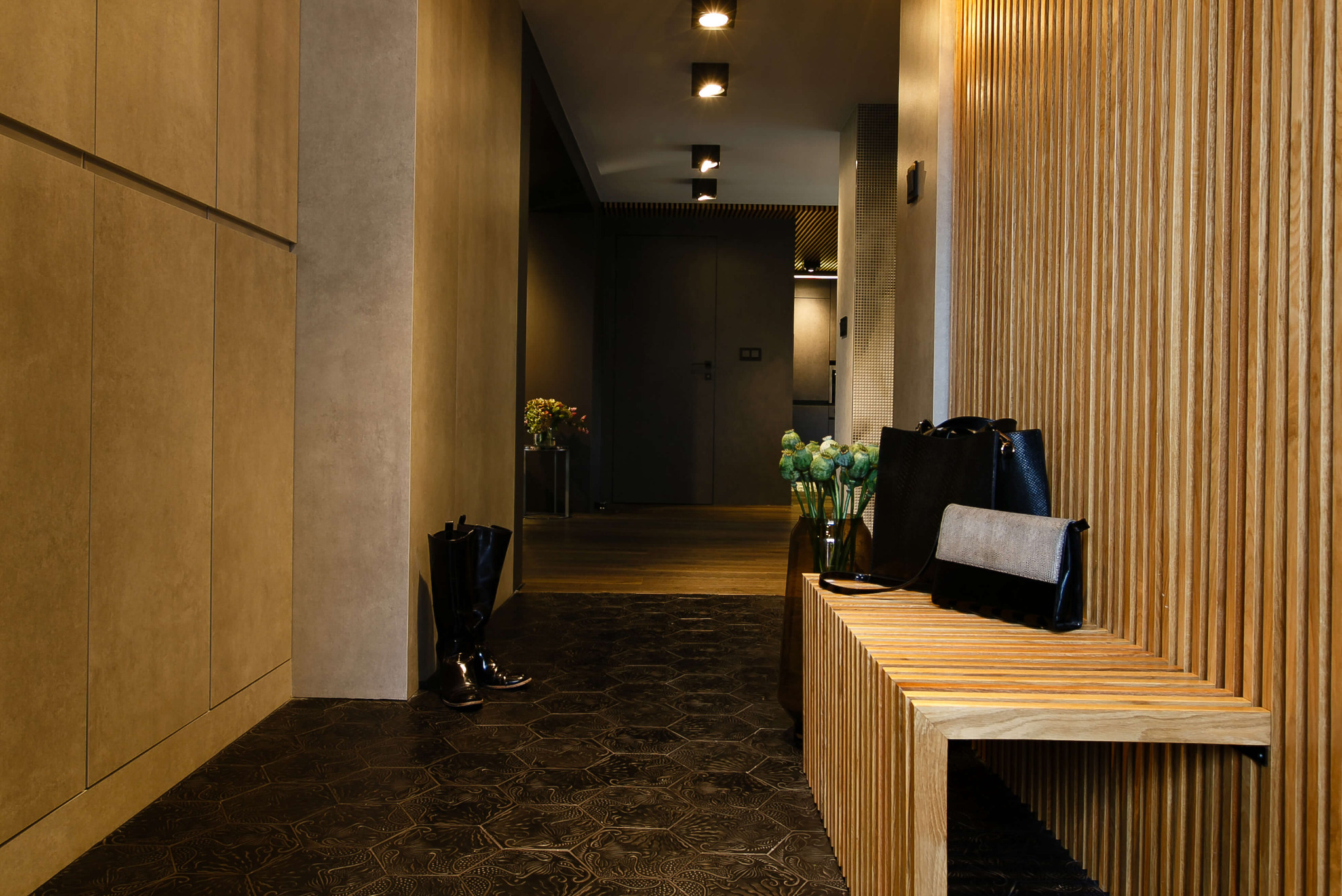 Nowoczesny przedpokój z drewnianą boazerią, heksagonalną podłogą z wzorem, niską ławką z torebkami, wysokimi butami i bukietami kwiatów w wazonach.