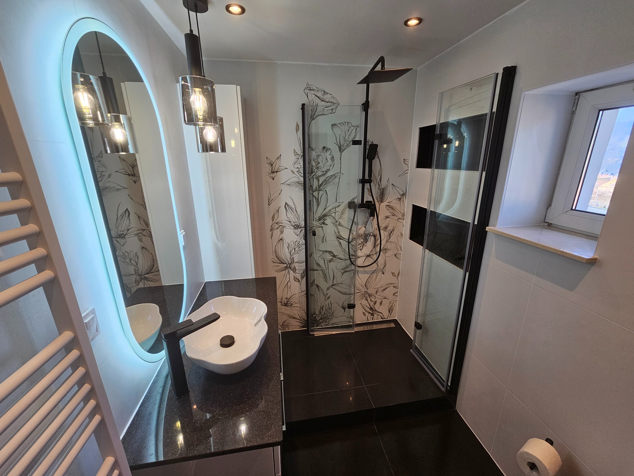 Nowoczesna łazienka z czarną armaturą, kabiną prysznicową typu walk-in i umywalką nablatową. Na ścianie dekoracyjne płytki z motywem kwiatowym.