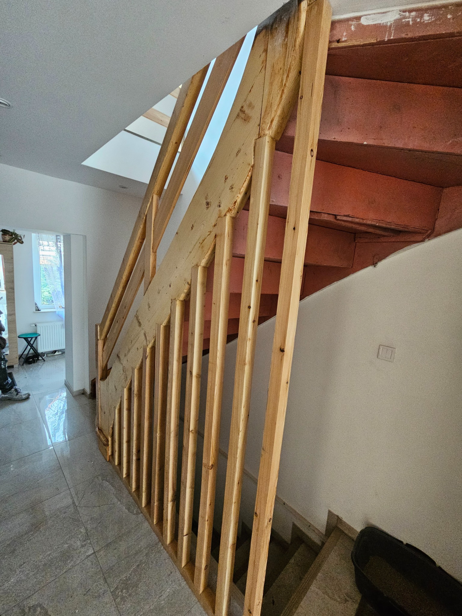 Surowe drewniane schody z balustradą w jasnym wnętrzu. Widoczne niedokończone elementy i surowe wykończenie. Ujęcie z dołu, podkreślające konstrukcję schodów.