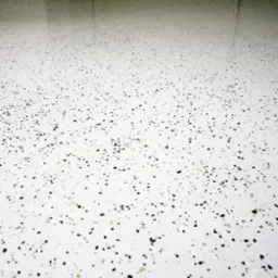 Biała posadzka przemysłowa z czarnymi i beżowymi drobnymi plamkami, widoczny połysk i odbicie światła.